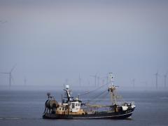 Vissersboot op zee met op de achtergrond windturbines