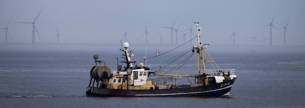 Vissersboot op zee met op de achtergrond windturbines