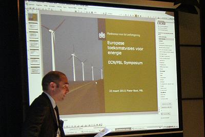 Foto van PBL directeur Maarten Hajer met op de achtergrond een presentatiedia met windmolens.